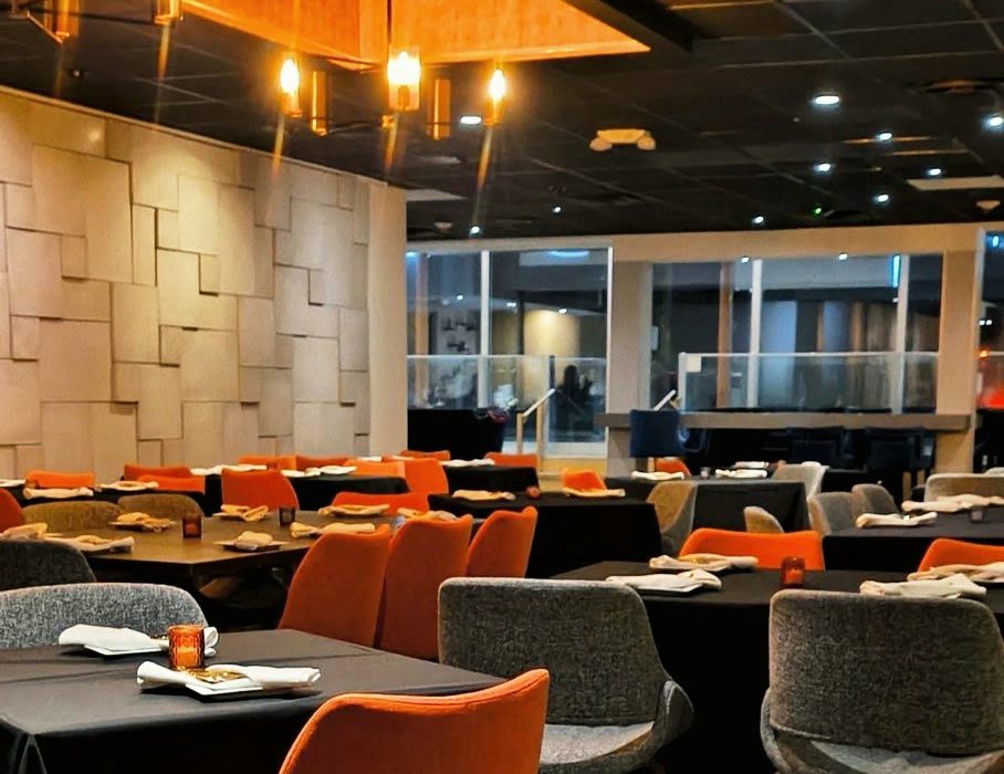The Saffron dining room set for service, with orange and grey chairs at black-linen tables under brass chandeliers
